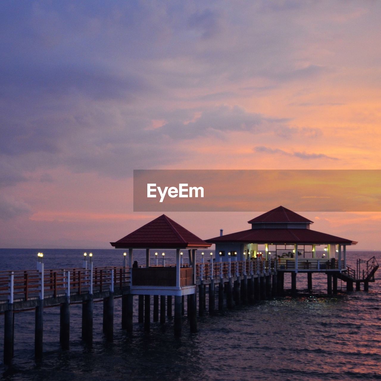 Stilt house on beach against sky during sunset