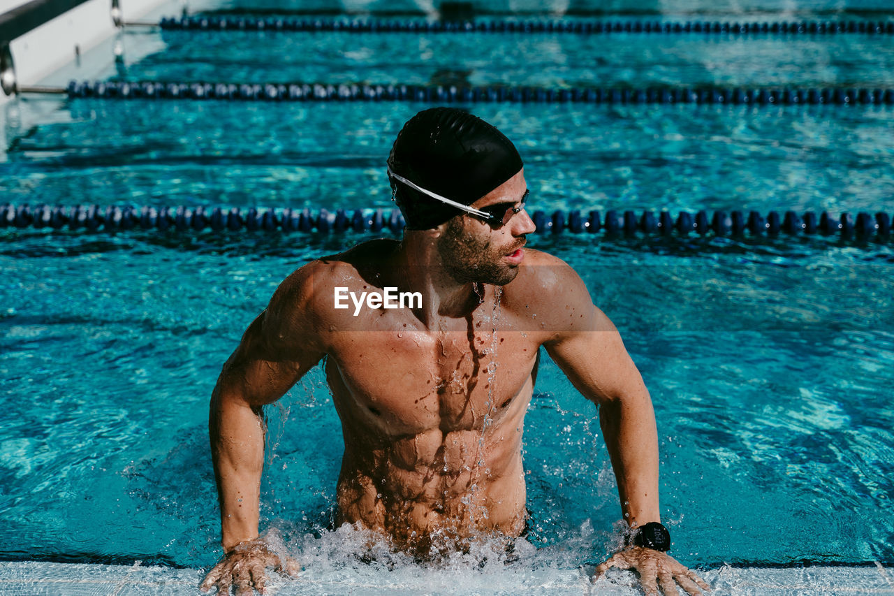 Muscular male swimmer looking away while standing at poolside