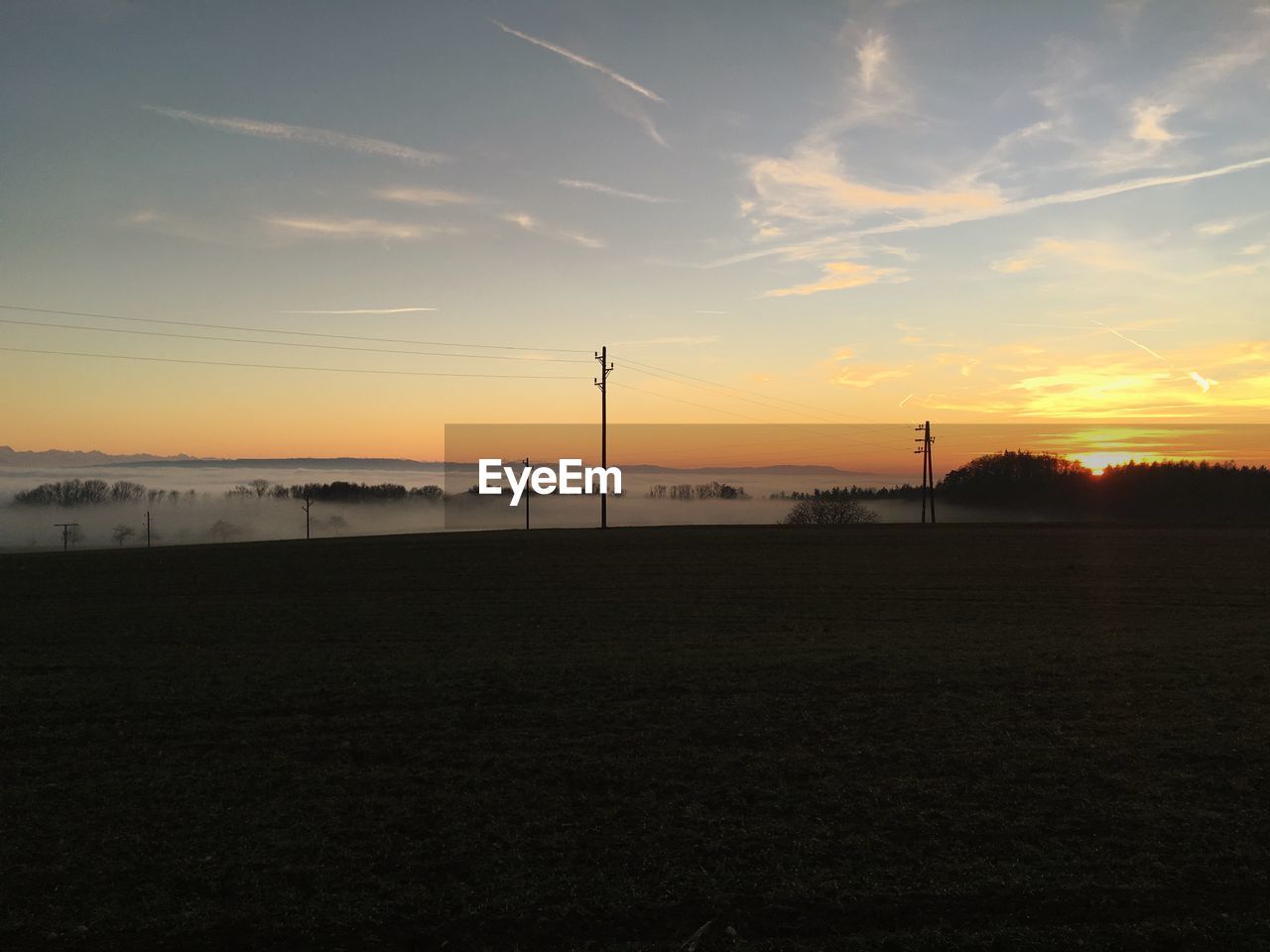 SILHOUETTE OF ELECTRICITY PYLON ON FIELD AGAINST SKY DURING SUNSET