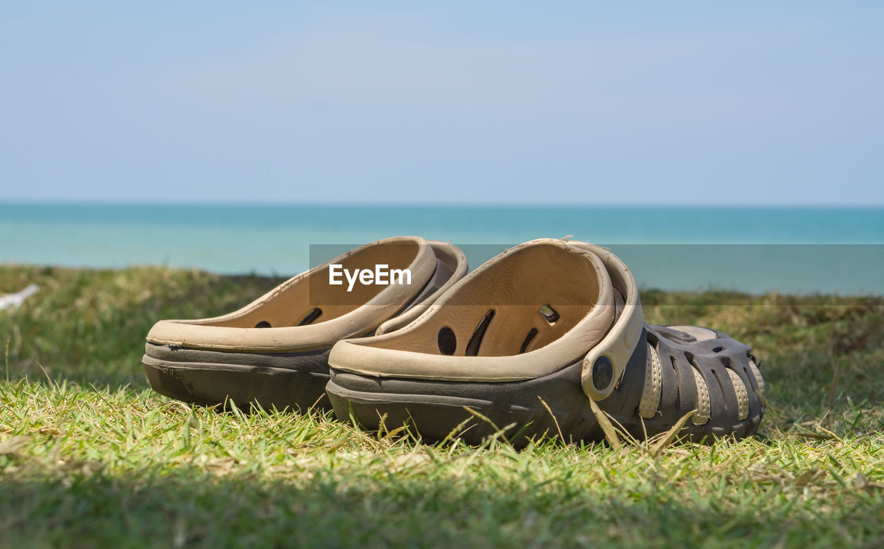 Abandoned shoes on grass by sea against sky