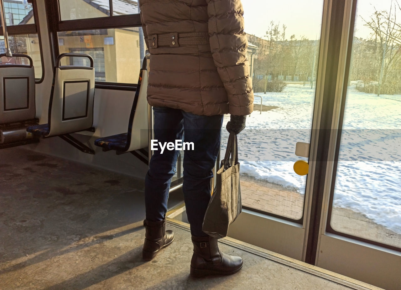 LOW SECTION OF MAN STANDING BY GLASS WINDOW