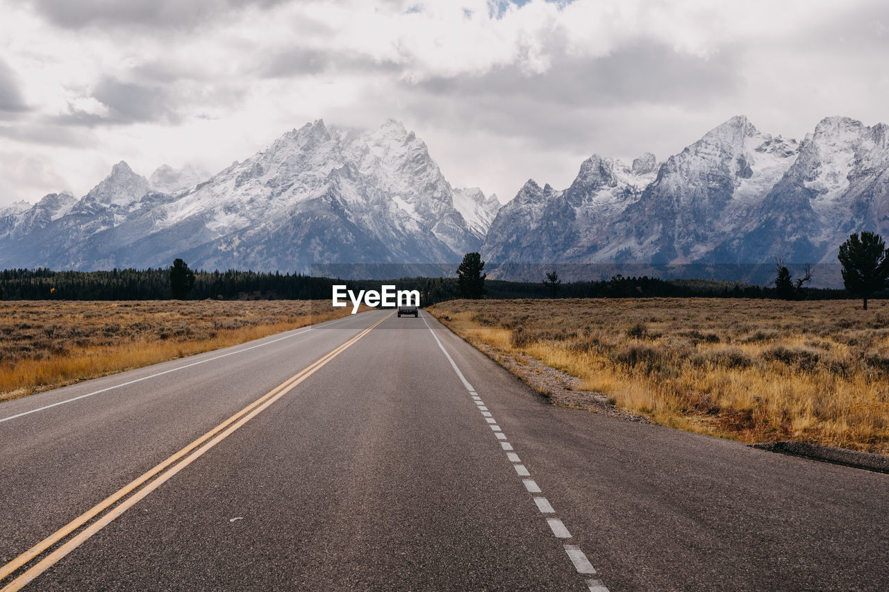 Road leading towards snowcapped mountains against sky