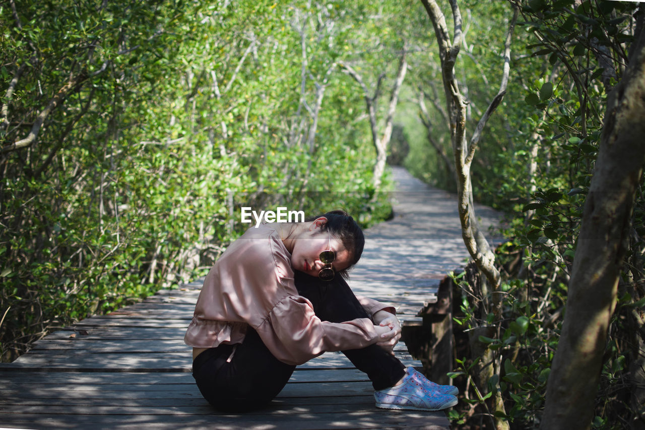 Side view of young man sitting on land in forest