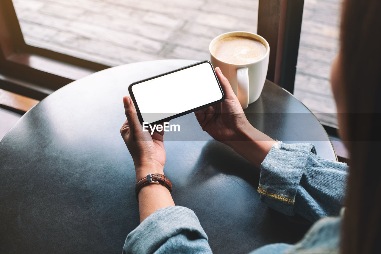 Cropped image of woman using blank phone at table in cafe