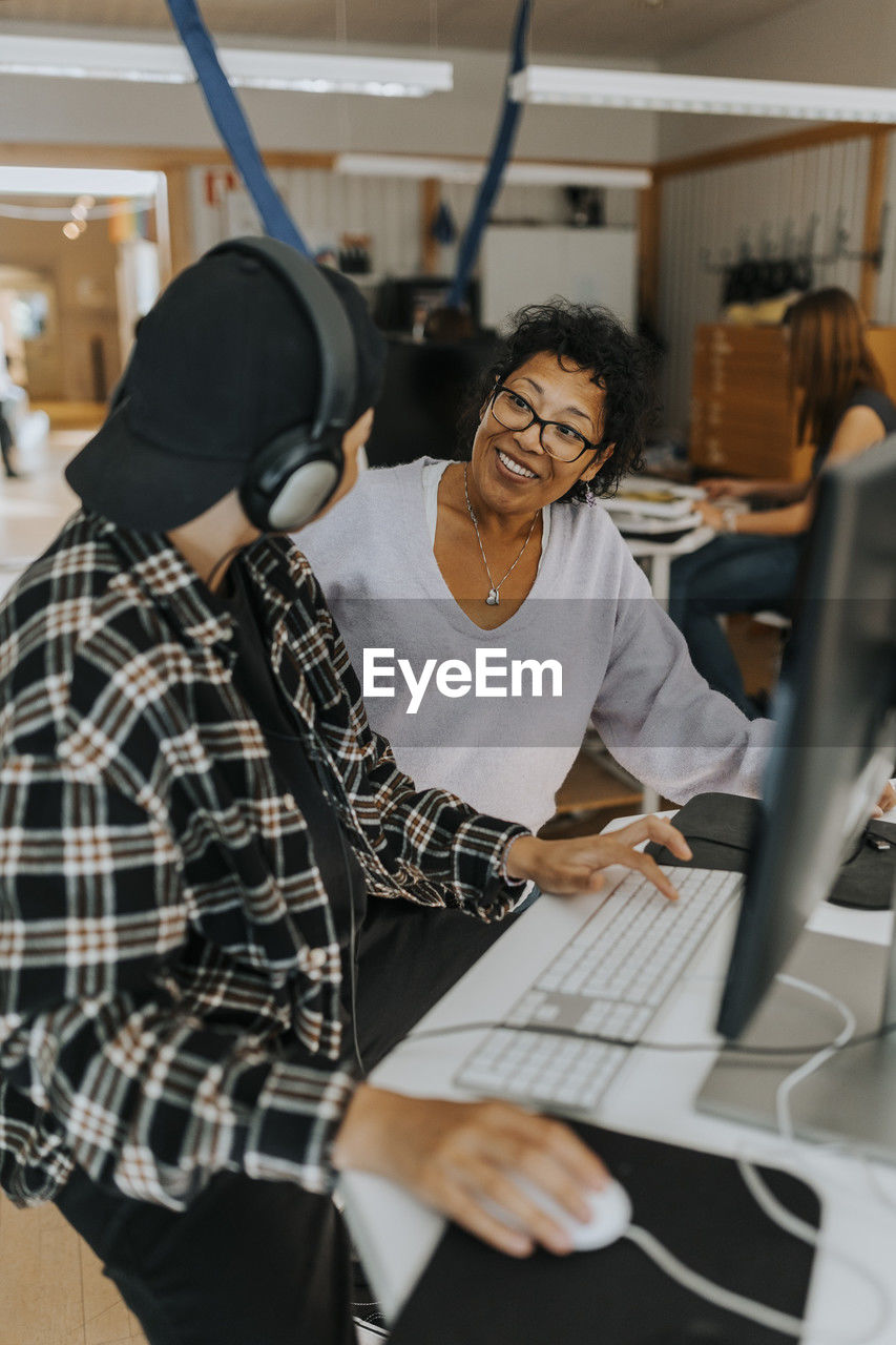 Smiling teacher looking at young male student in computer lab