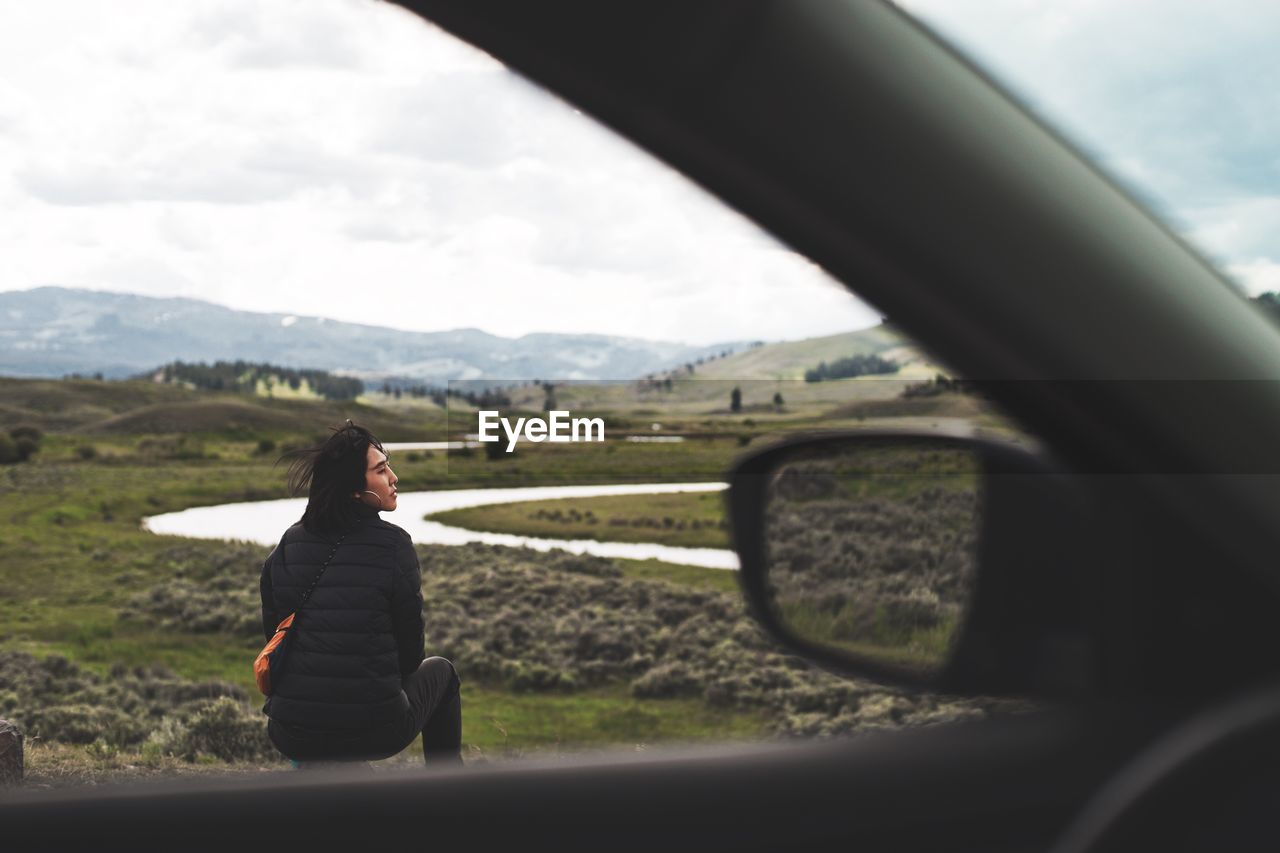 Rear view of woman sitting on landscape seen through car 