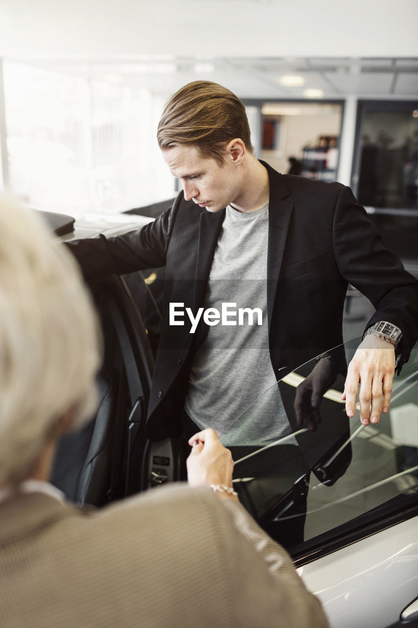 Man examining car with saleswoman in foreground at shop