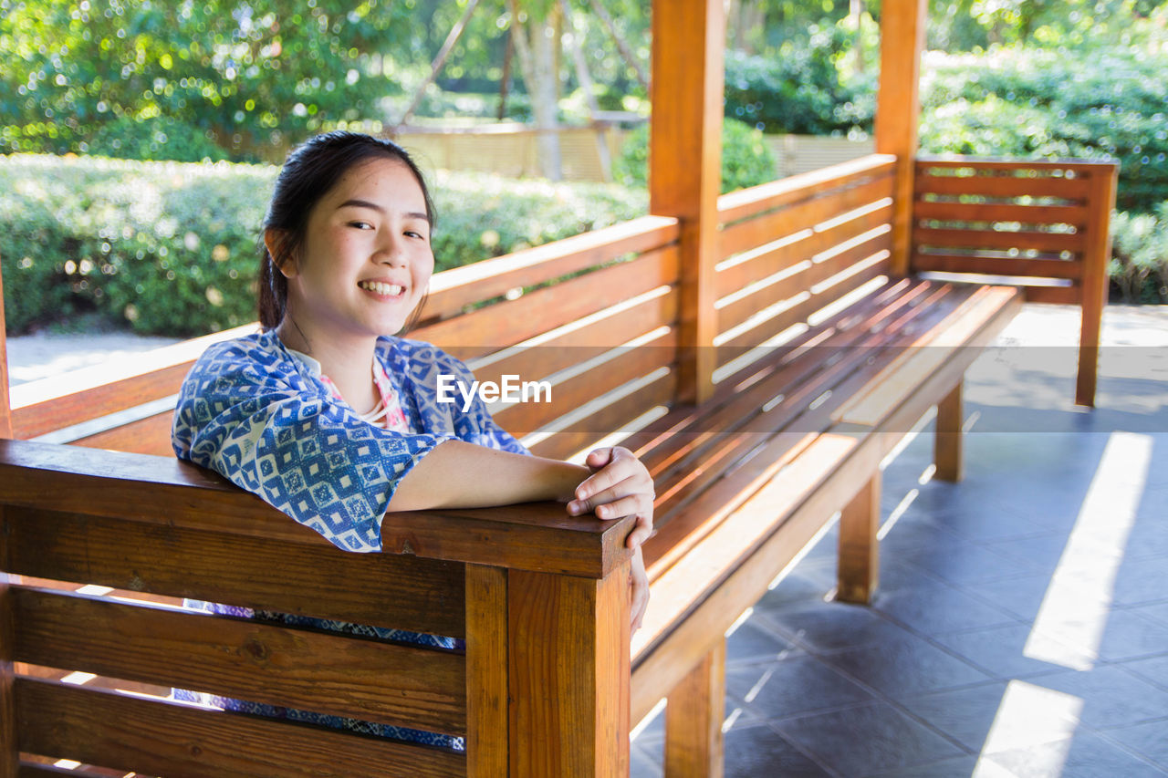 Portrait of smiling woman sitting on bench in park
