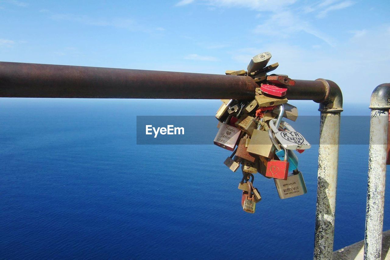 Love padlocks handing on railing against blue sea