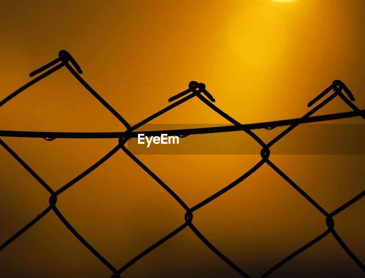 Close-up of silhouette chainlink fence against sky during sunset