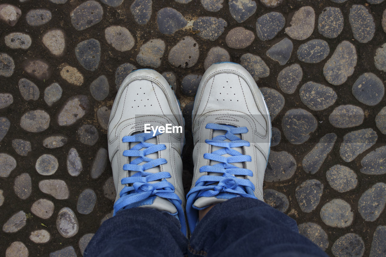 LOW SECTION OF PERSON WEARING SHOES STANDING ON COBBLESTONE