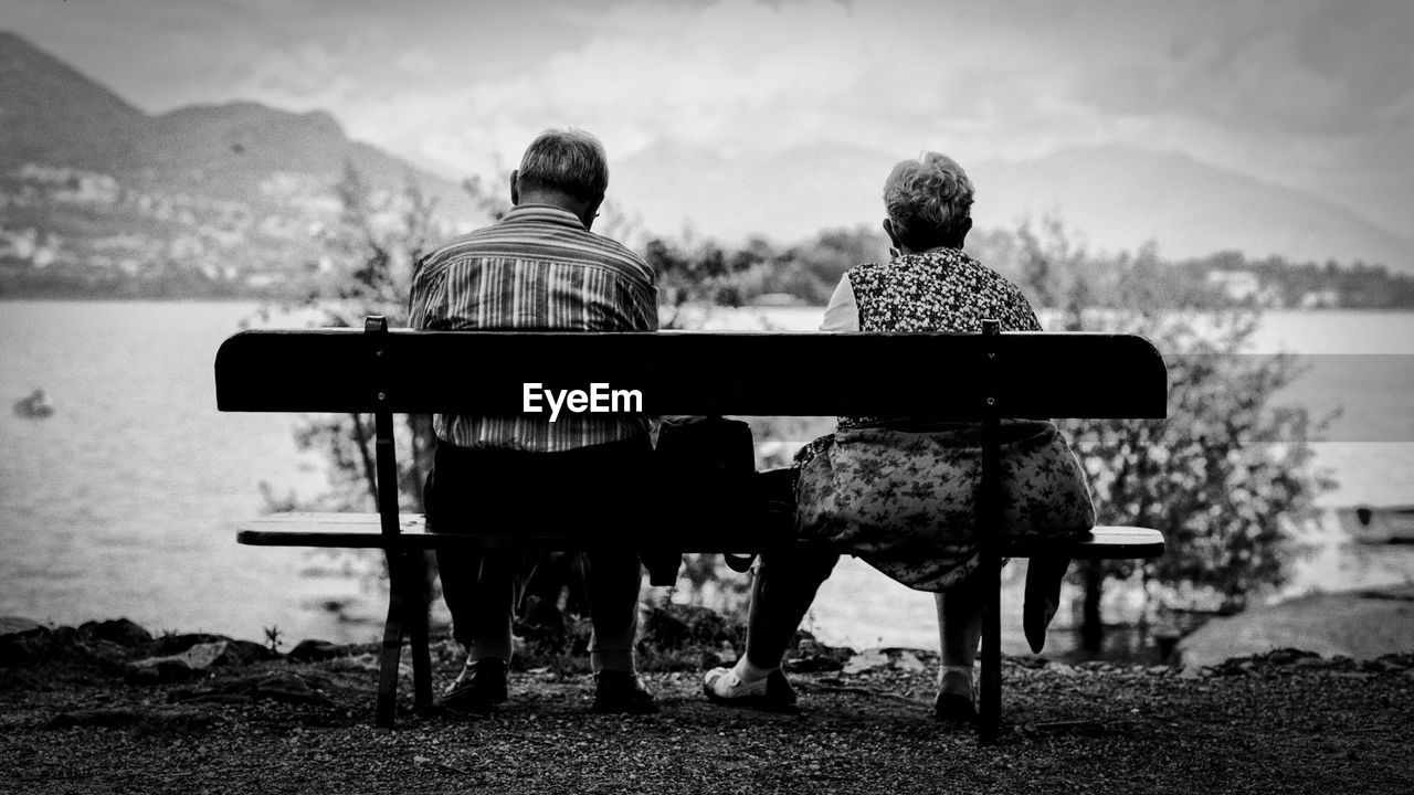 Rear view of couple sitting on bench by lake