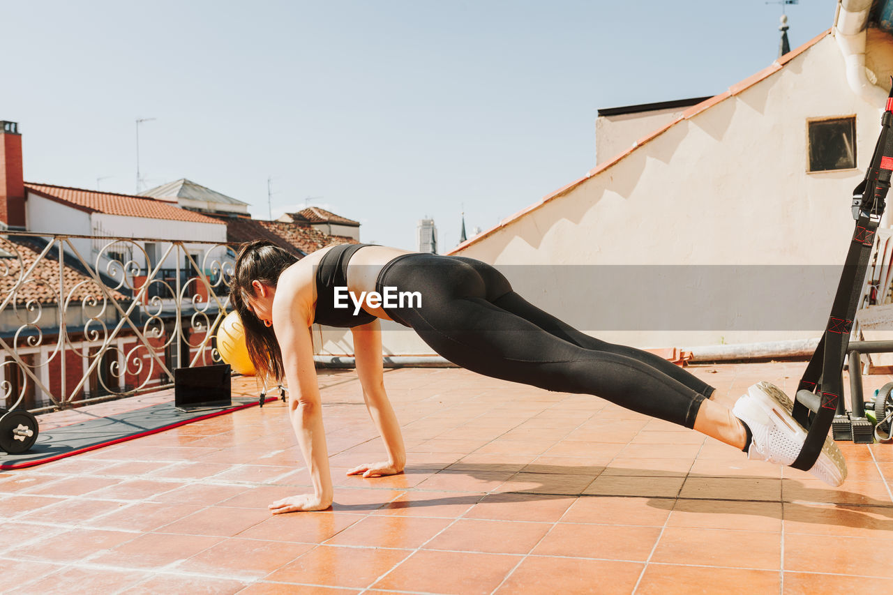 Woman doing urban workout for arms and chest with trx fitness straps. 