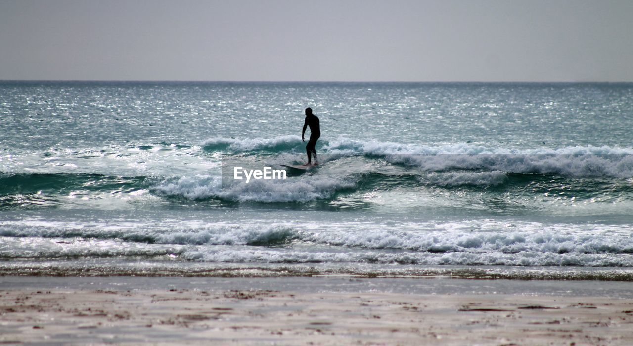 Silhouette surfer surfing in sea against clear sky