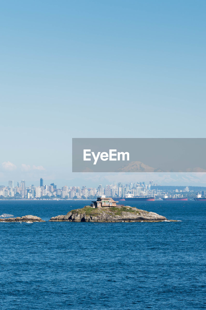 House on rock formation amidst sea against city