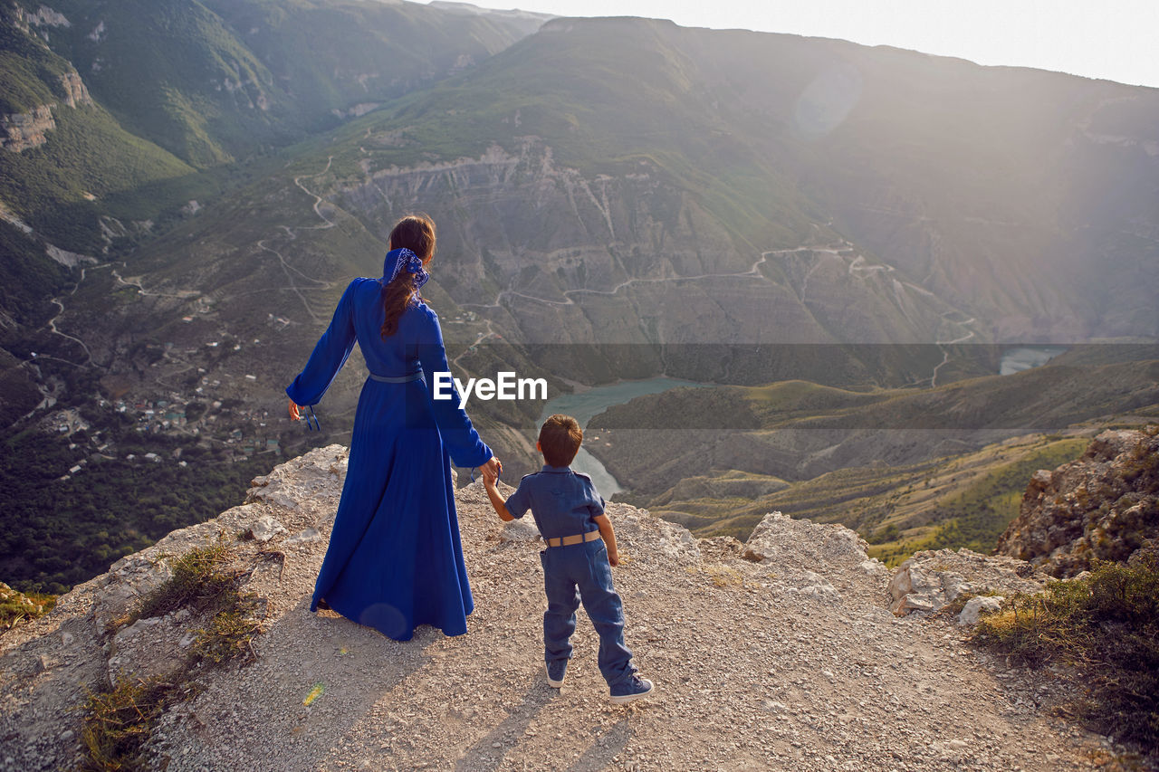 Mother in a blue dress with her son stands on the cliff of the sulak canyon