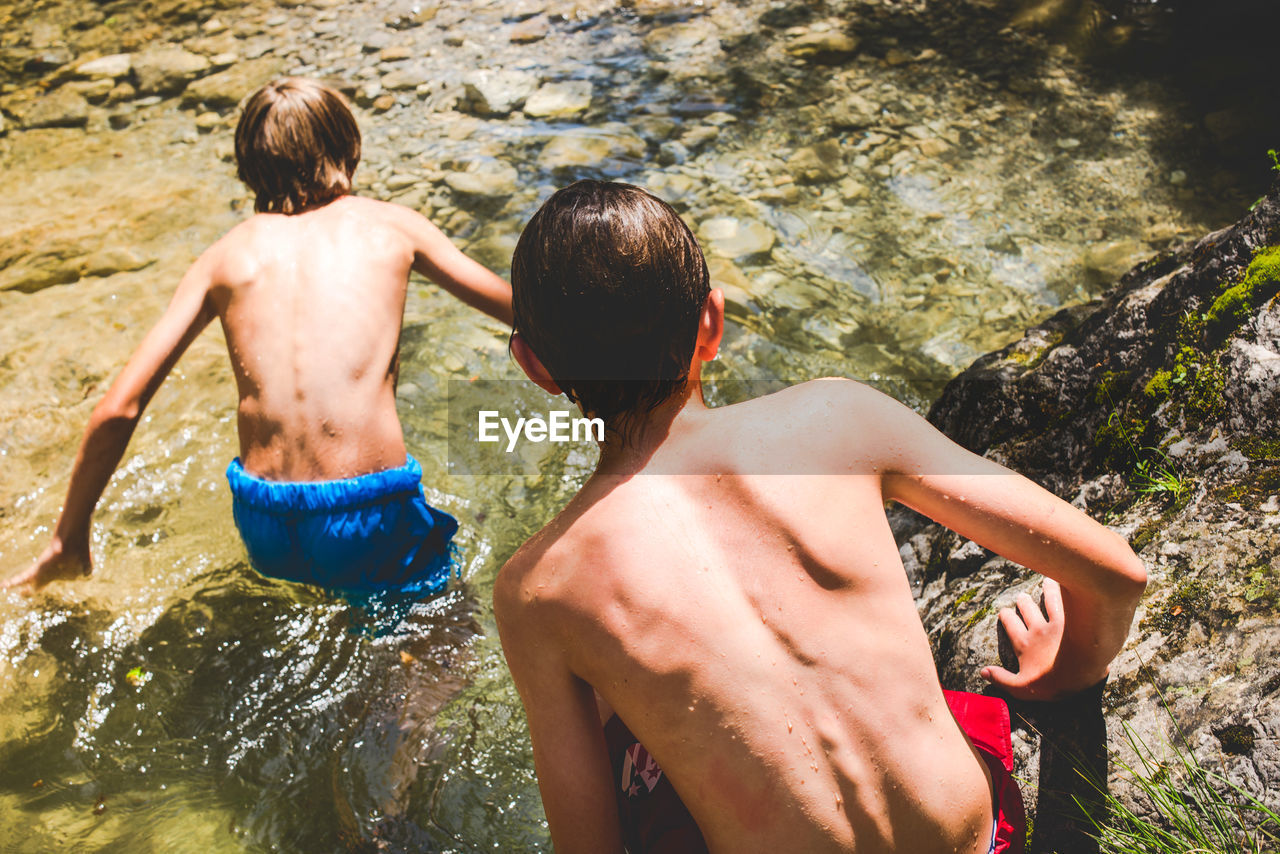 Rear view of shirtless boys in water