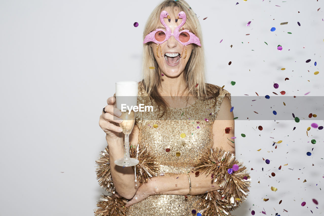 Senior woman wearing golden dress and flmingo shaped glasses, celebtraing new year's eve