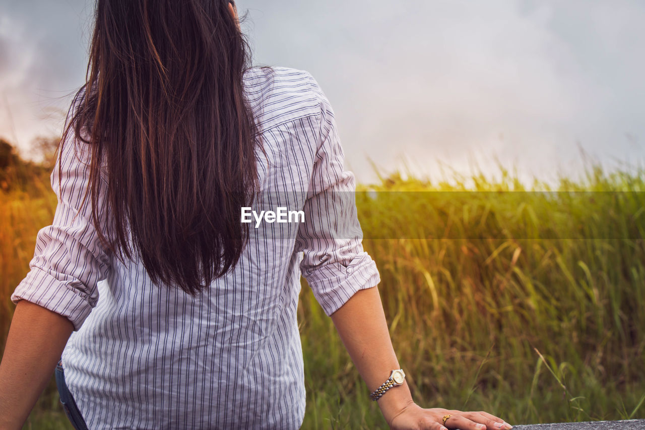 Rear view of woman sitting on field against sky