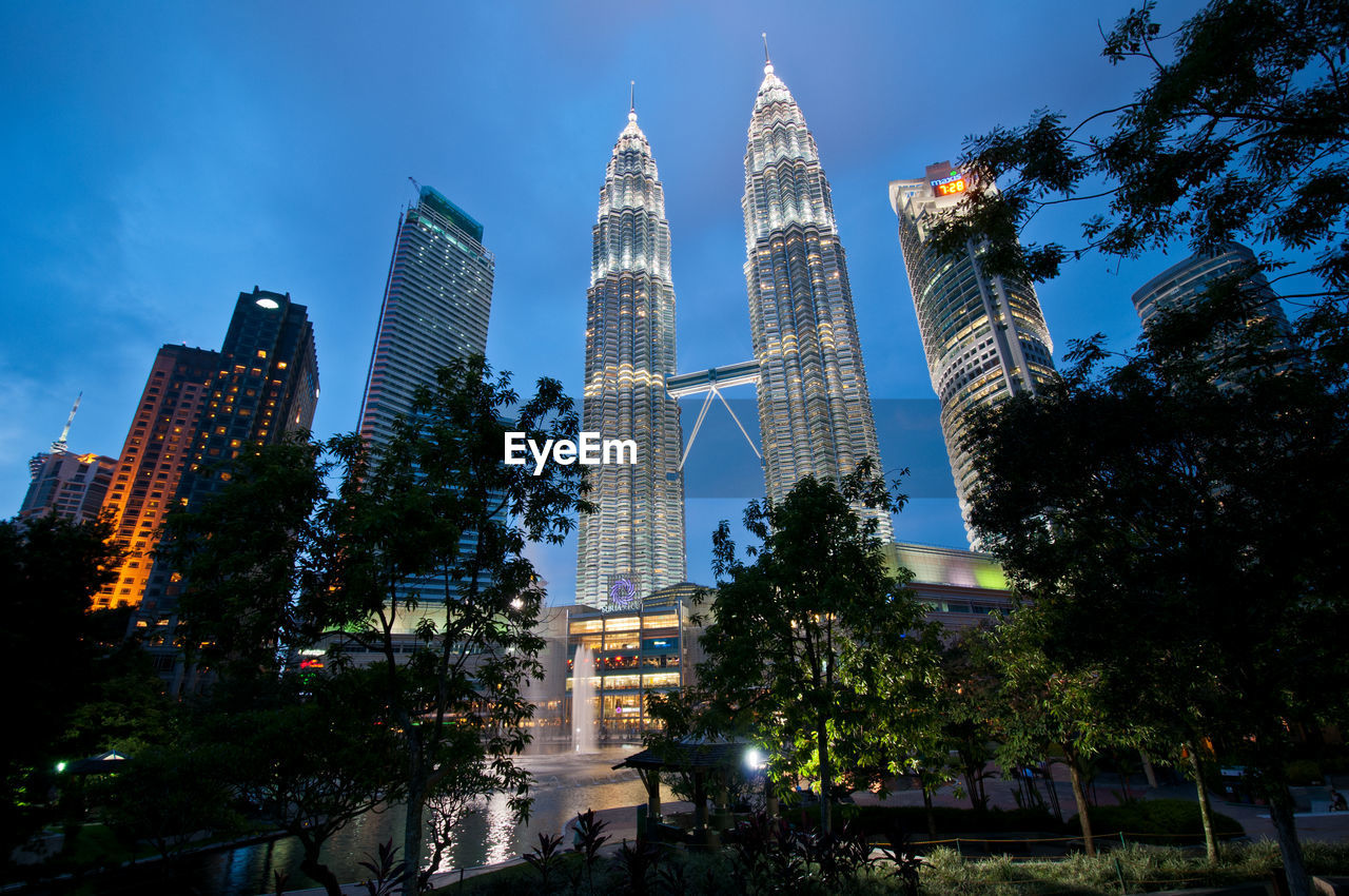 Low angle view of trees and illuminated skyscrapers