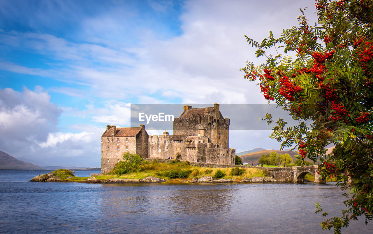 Historical buildings by river against cloudy sky