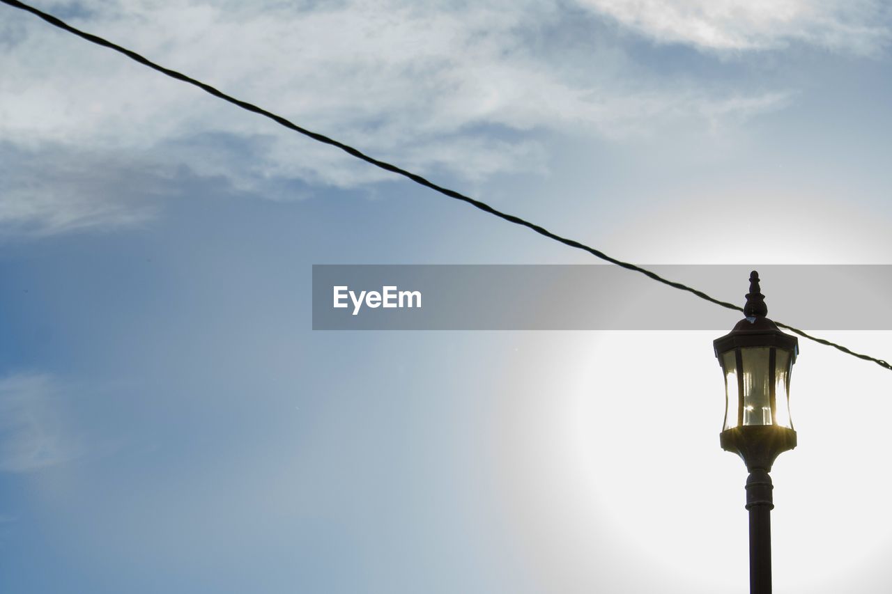 Low angle view of lamp post and cable against sky on sunny day