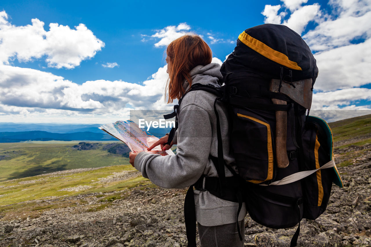 Stylish woman with backpack hiking, orient themselves to the terrain, study map and navigate 