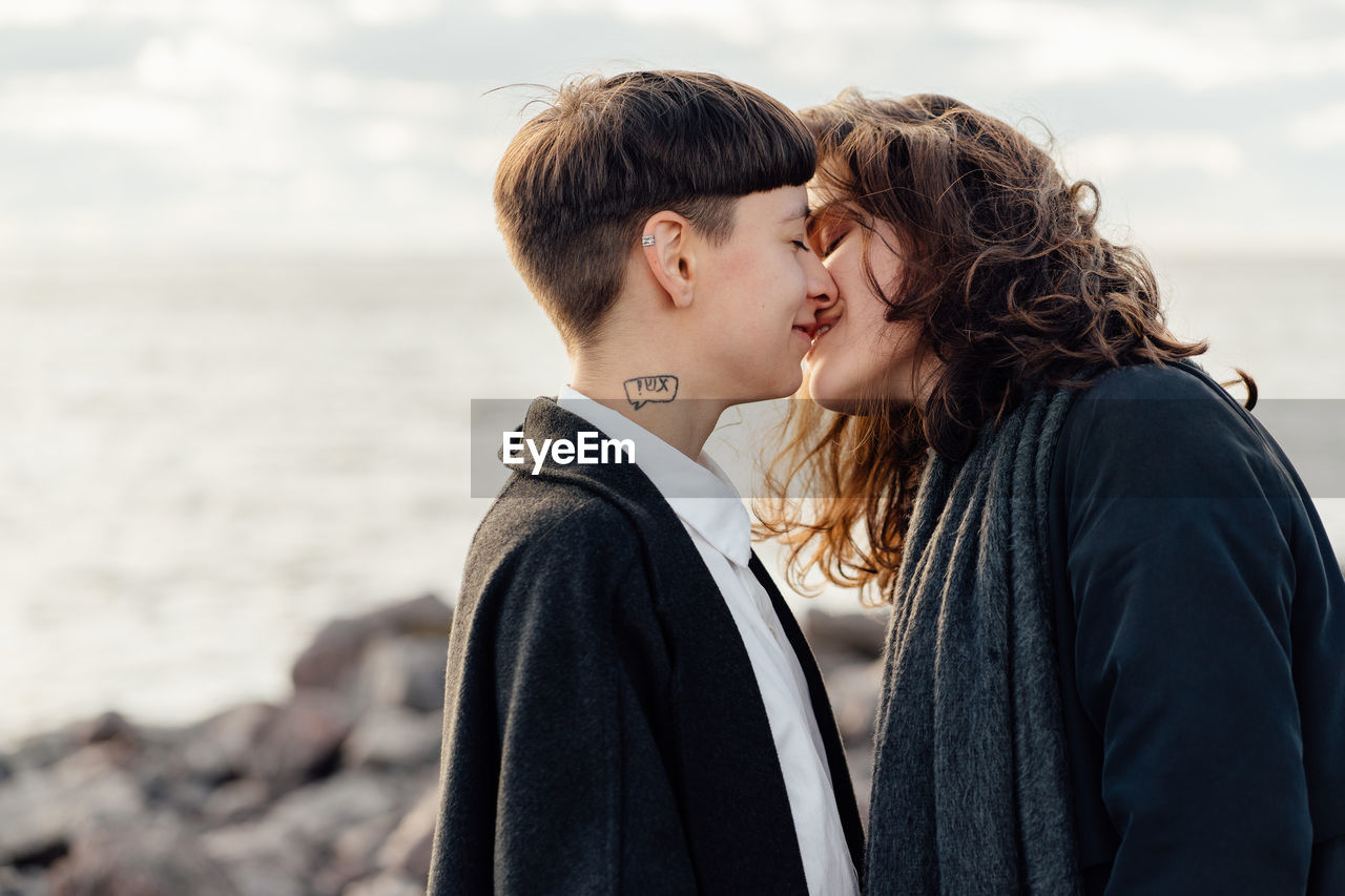 SIDE VIEW OF COUPLE KISSING AGAINST SEA