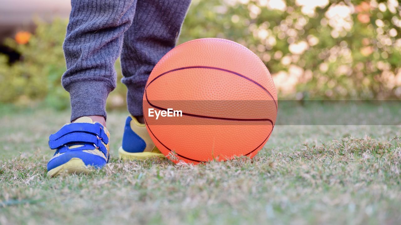 Low section of boy standing by basketball on field