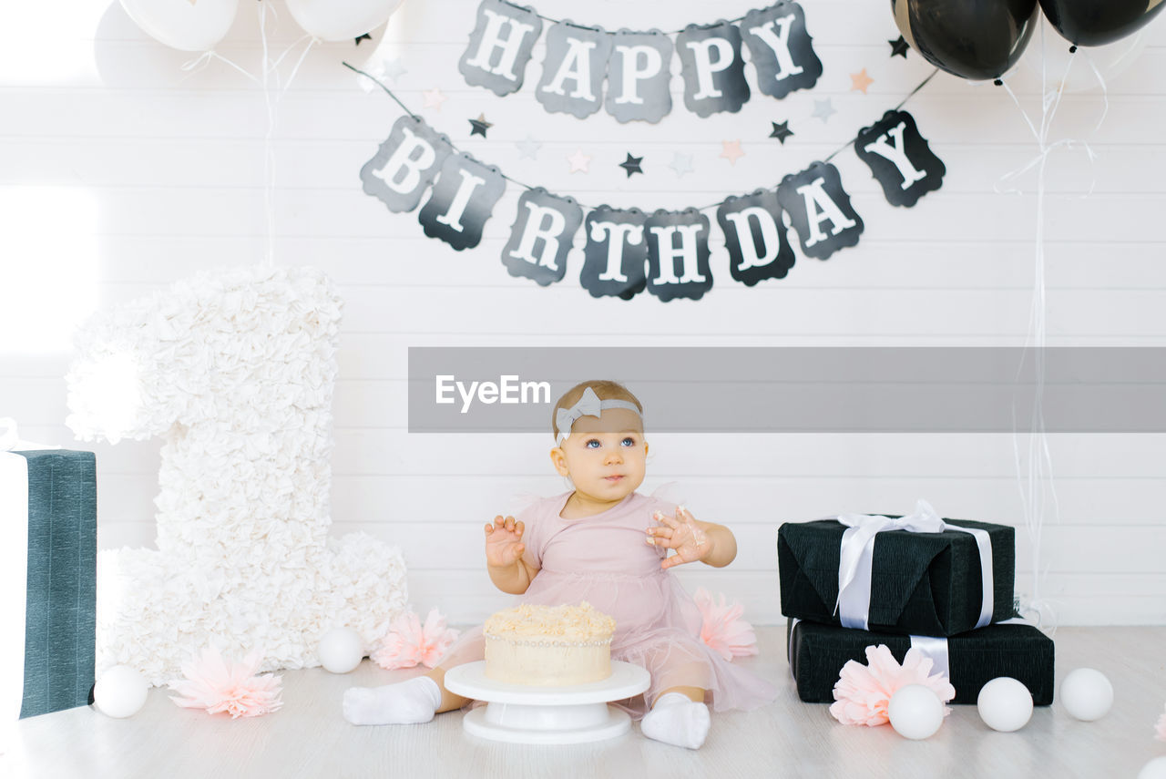 A one-year-old girl sits near a cake, celebrates her first birthday in a photo zone