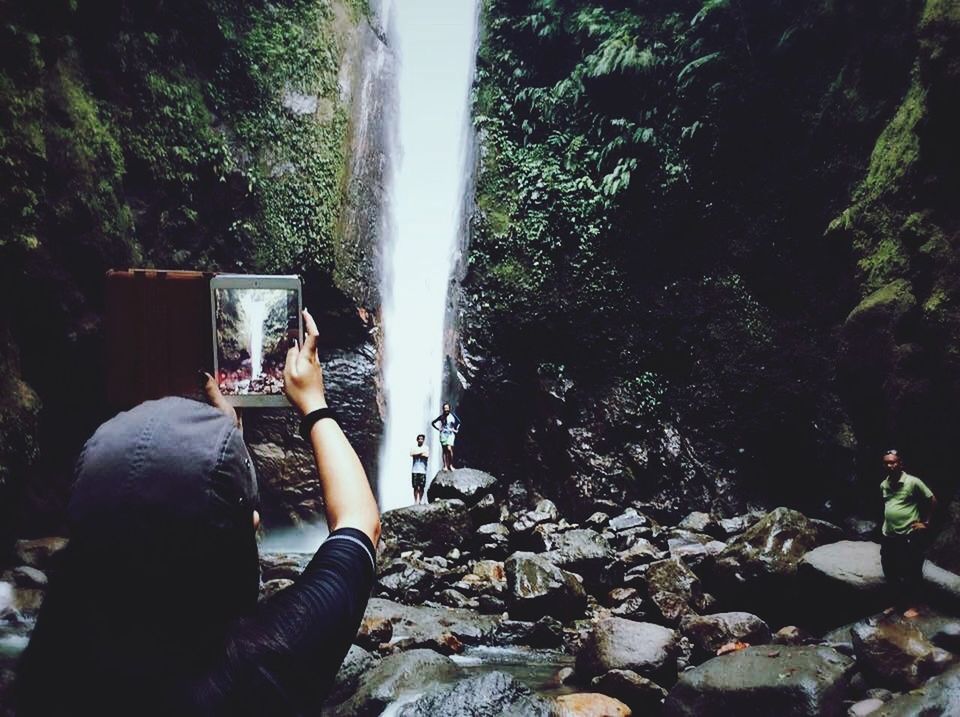 Woman taking picture of waterfall on digital tablet