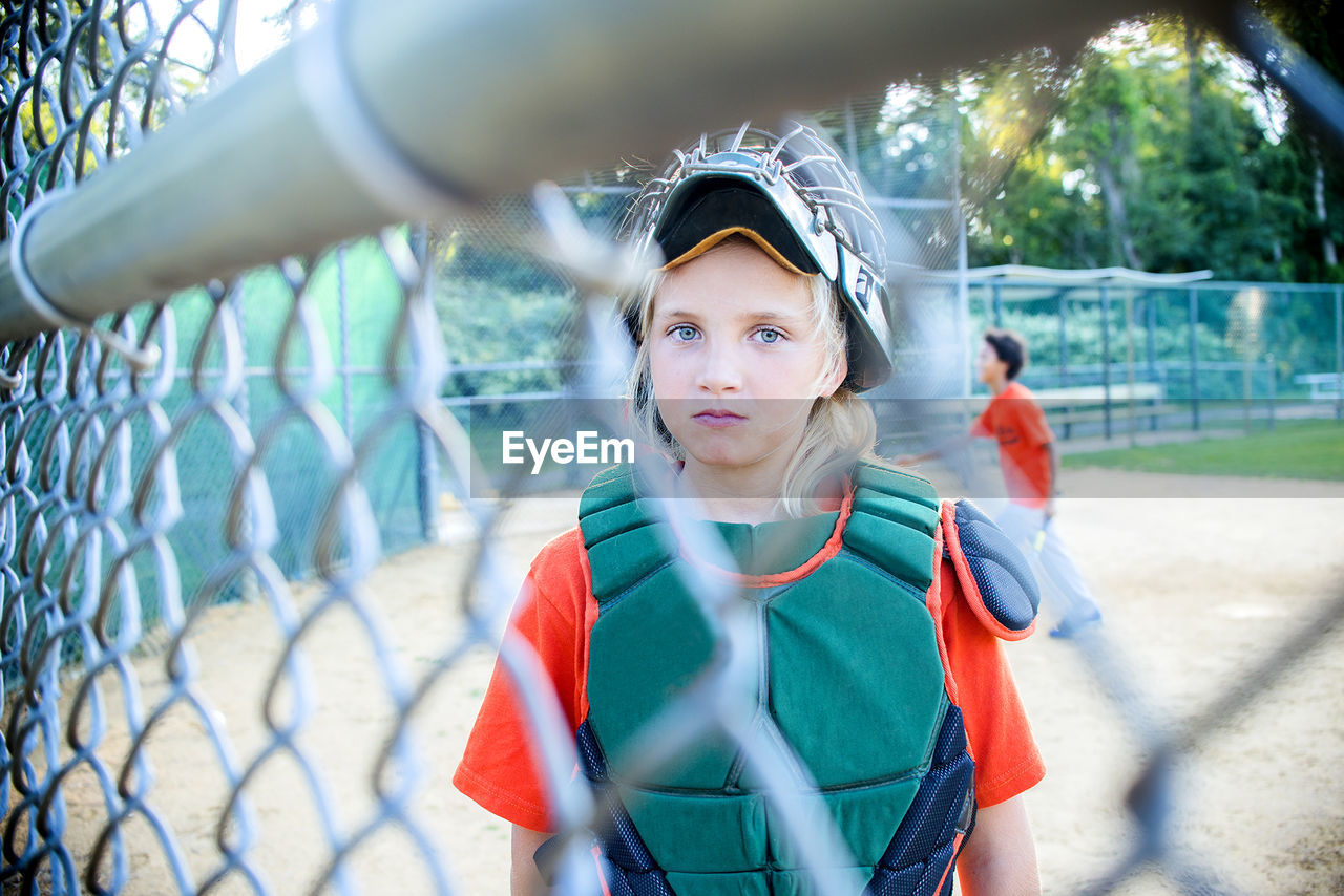 Portrait of girl standing at playing field seen through chainlink fence