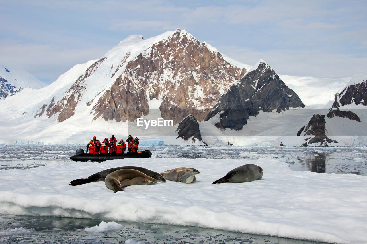 People in inflatable raft on sea by snowcapped mountain during winter