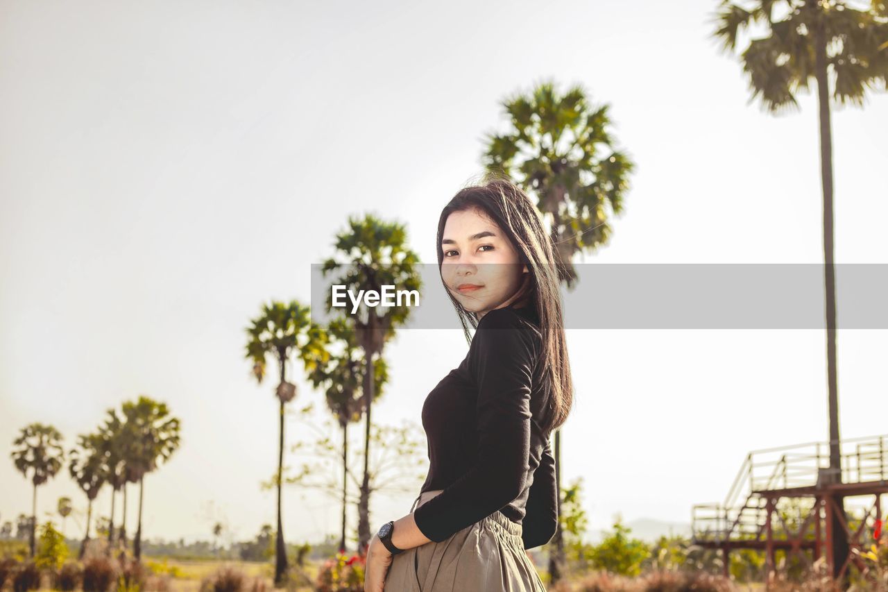 Portrait of beautiful young woman standing against sky