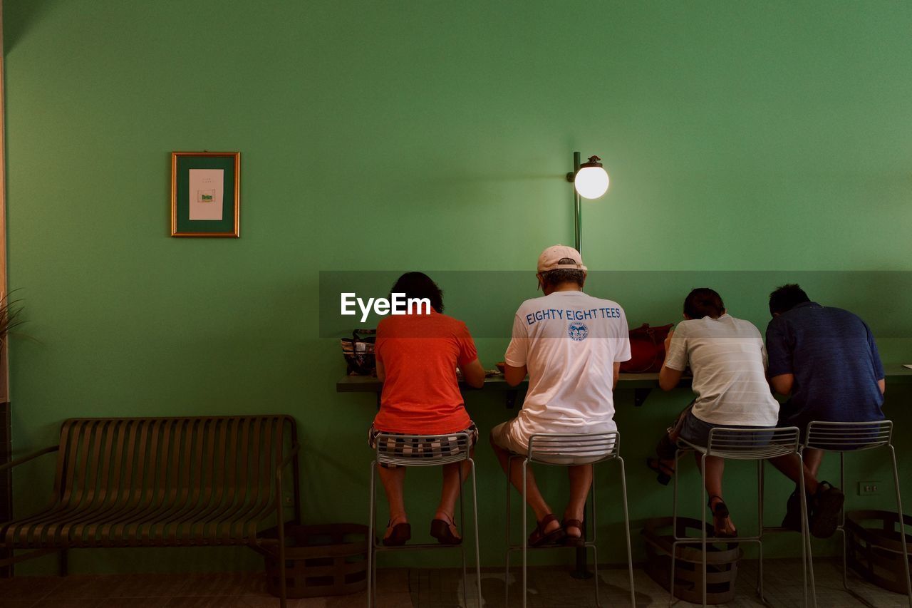 REAR VIEW OF PEOPLE SITTING ON WALL