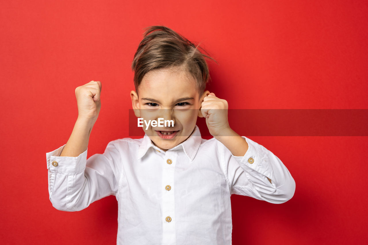 one person, childhood, child, portrait, colored background, studio shot, red, emotion, indoors, waist up, person, front view, looking at camera, fun, red background, smiling, toddler, happiness, men, cute, arm, facial expression, female, gesturing, women, hand, positive emotion, clothing, standing