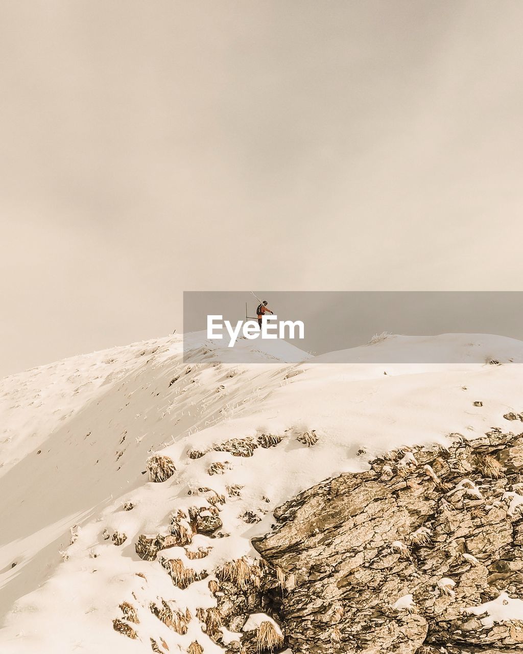 Scenic view of snow covered mountain against sky with skier peering over cliffs 