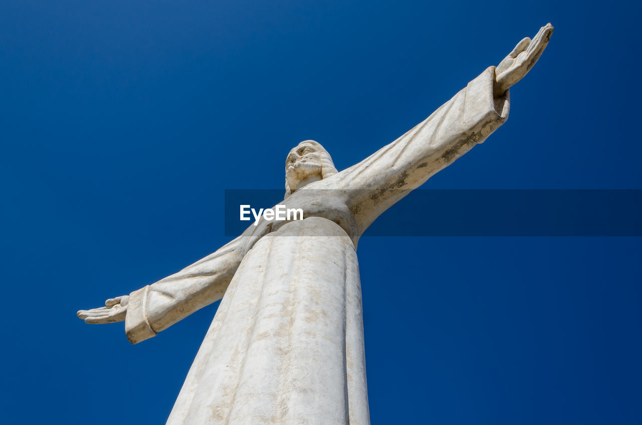 Low angle view of jesus christ statue against blue sky, lubango, angola