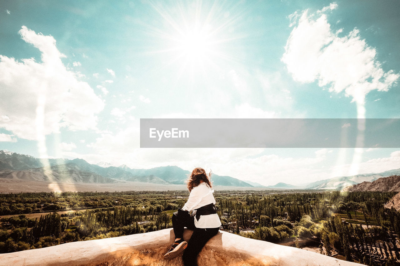 Side view of woman looking at landscape while sitting against sky on sunny day