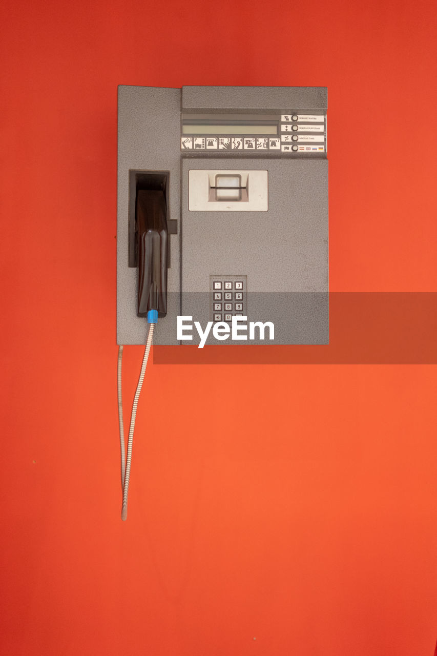 Close-up of telephone booth against orange wall