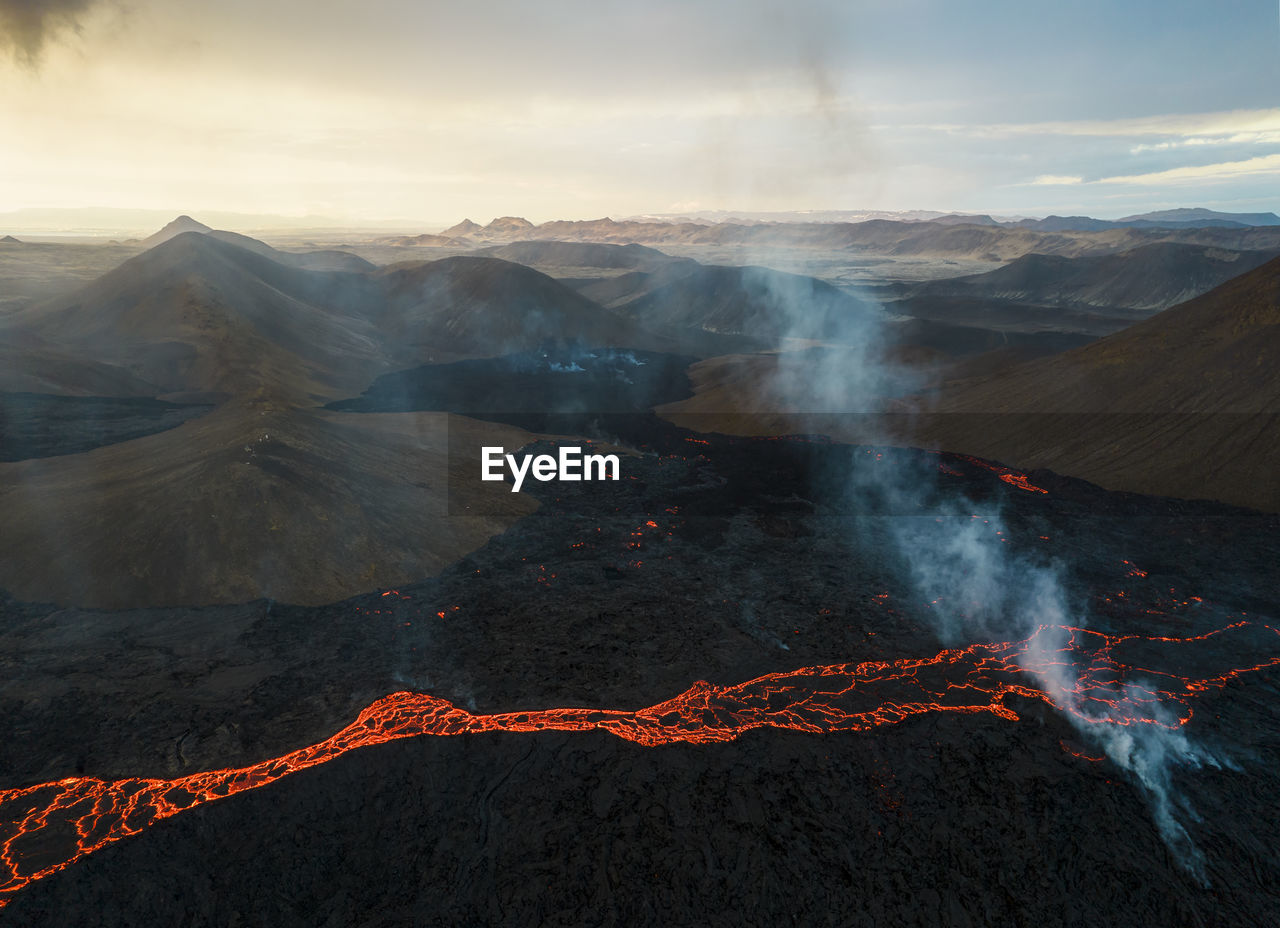 Drone view of stream of hot orange lava flowing through mountainous terrain in morning in iceland