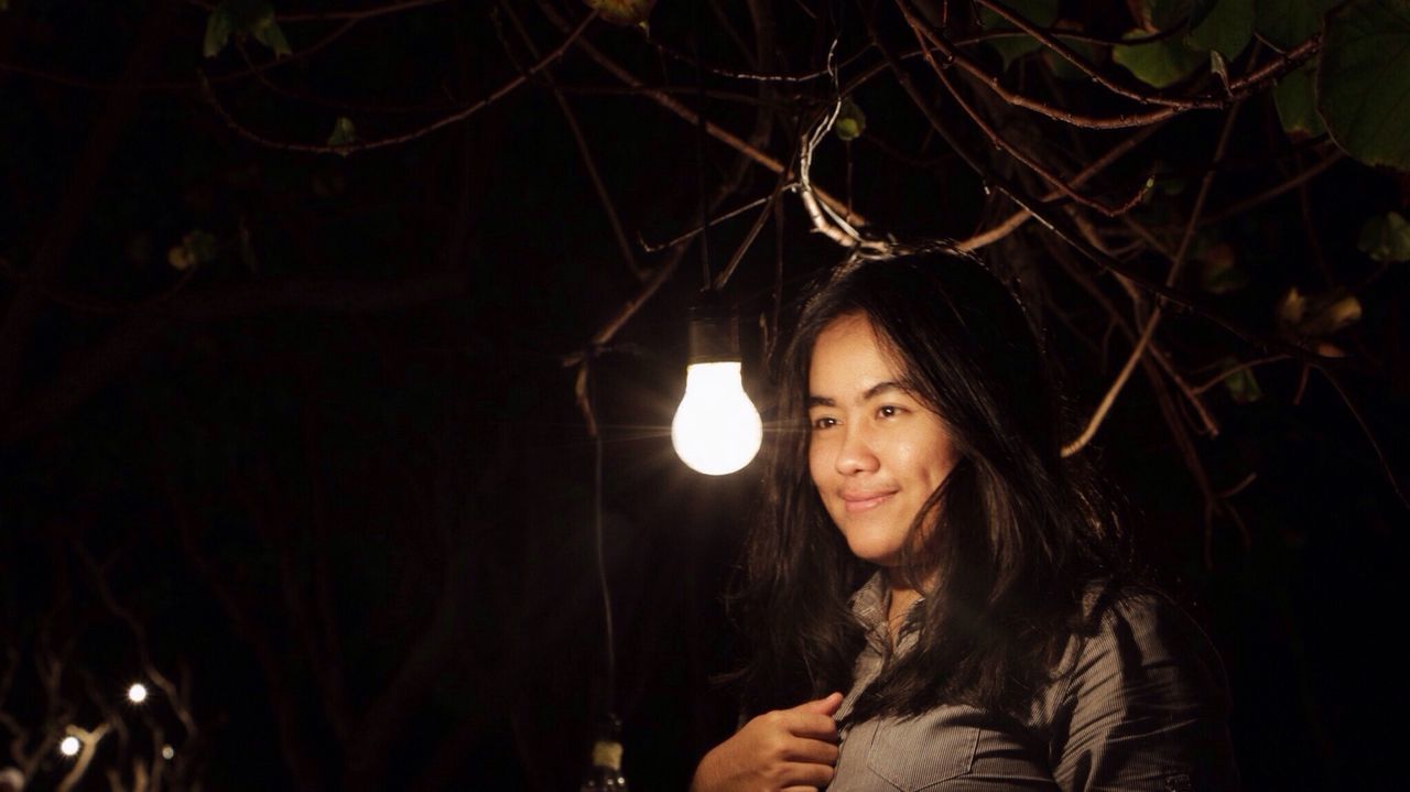 Smiling woman by illuminated light bulb at night