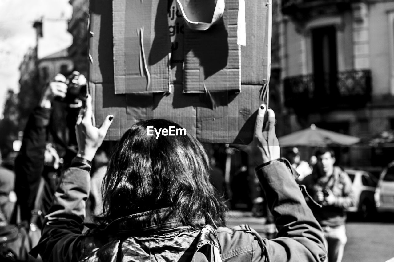 Rear view of woman holding information sign during protest in city