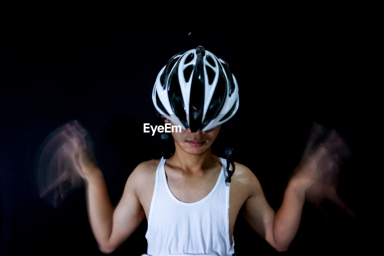 Close-up of man with blurred hands wearing bicycle helmet against black background
