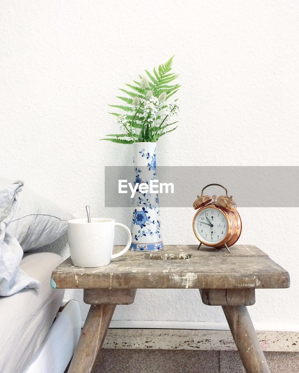 Clock and vase on wooden table against wall