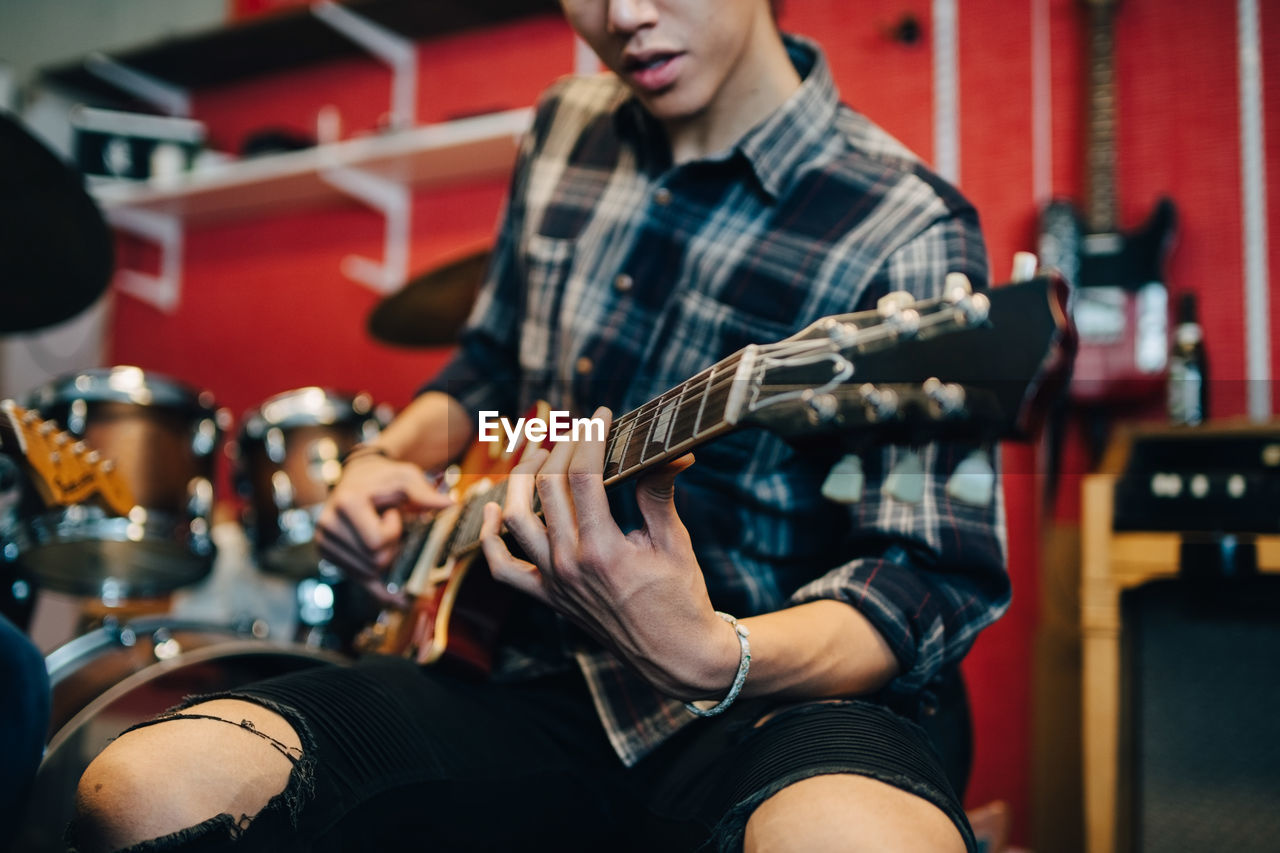 Midsection of man playing guitar while sitting in recording studio