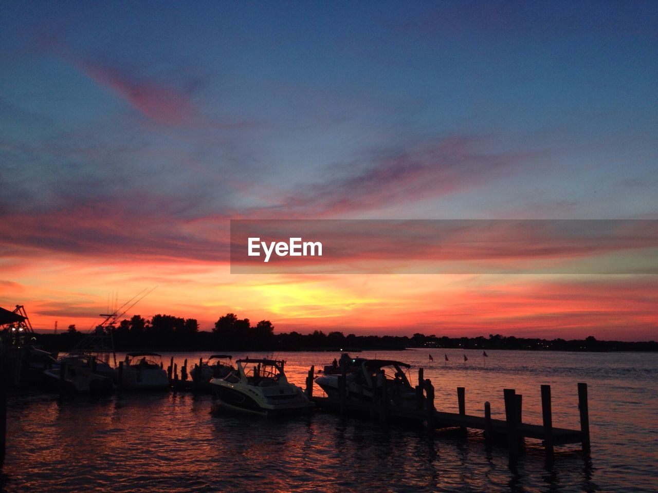 Boats moored in harbor on lake against sky during sunset