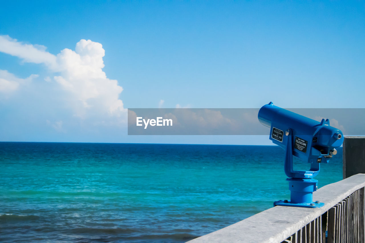 Blue coin-operated binoculars at observation point by sea against sky