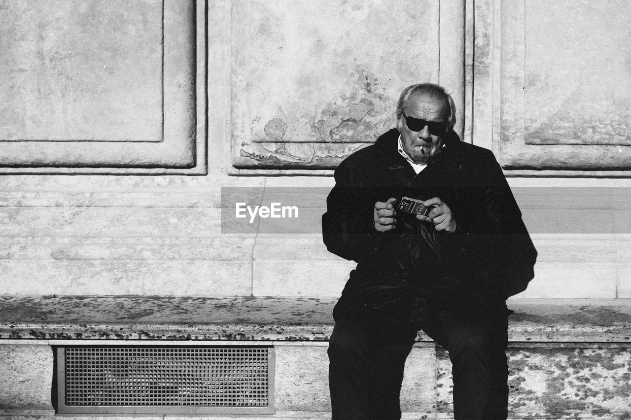 Senior man smoking while sitting on seat against wall