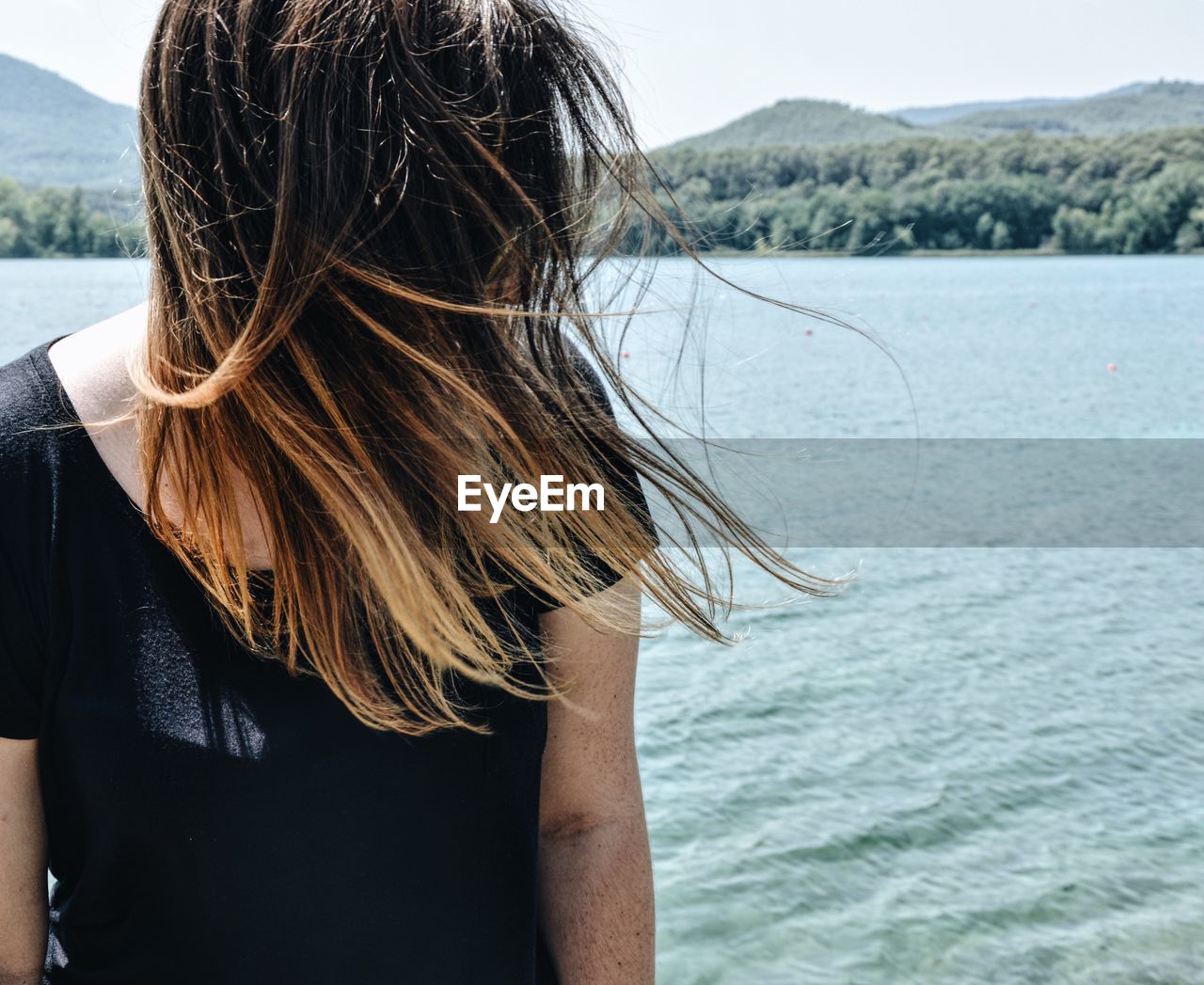 Woman with tousled blond hair against sea on sunny day